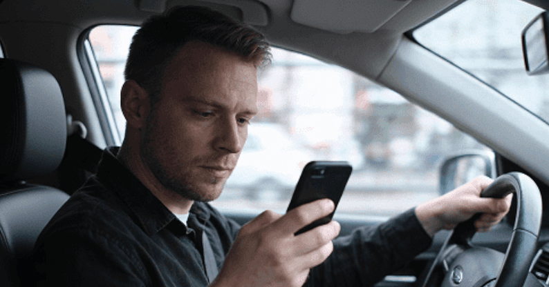 Conductor revisando el celular al volante, captado por la cámara con IA